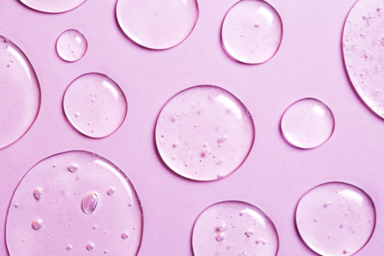 Drops of Niacinamide on a pink background. Learn what niacinamide does for your skin.